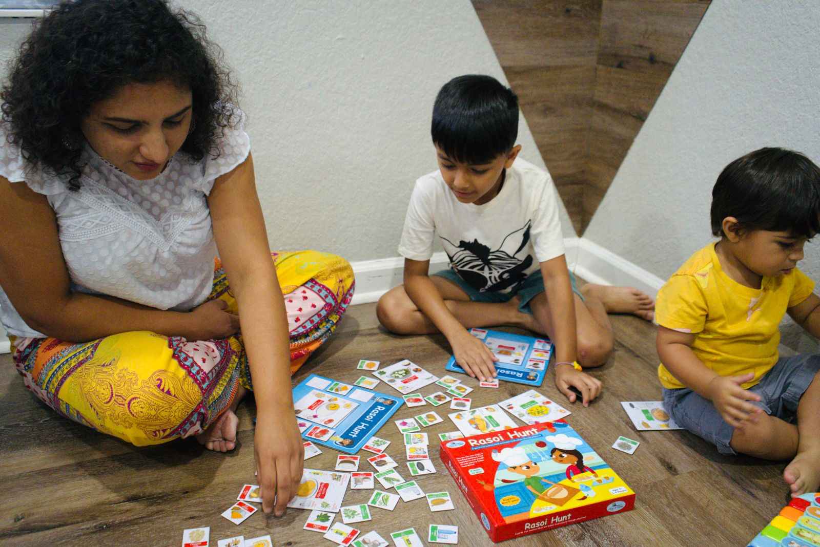 Children and adult playing Rasoi Hunt game by PlayNSeekh. Players are looking through the scattered magnetic tiles of Indian food ingredients to make the popular Indian food dishes. 