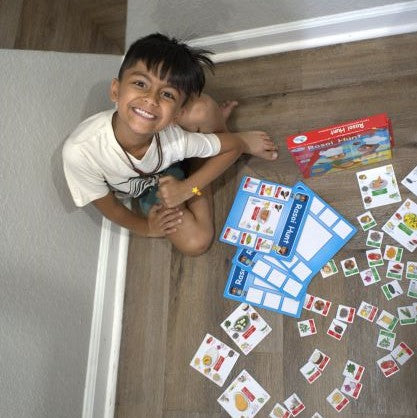 Child smiling and having fun playing Rasoi Hunt. Magnetic titles of Indian food ingredients are food dishes are scattered. 